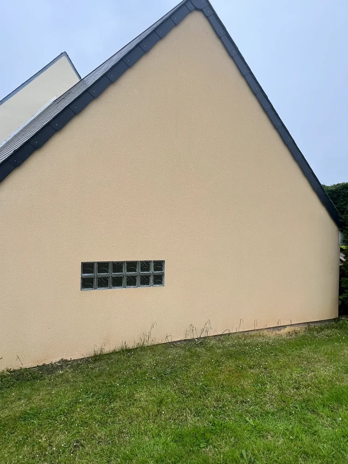 Le même pignon à l'enduit beige propre et uniforme après nettoyage, mêmes briques de verre, plus aucune coulure