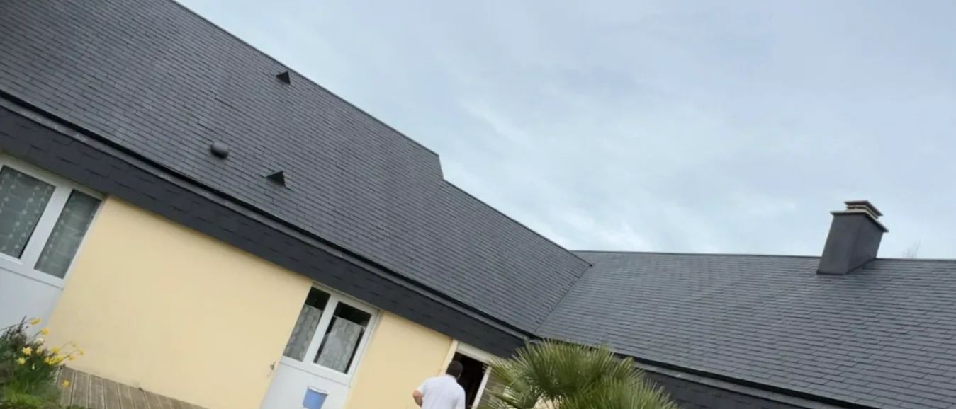 La même toiture en ardoise redevenue noire et nette après nettoyage, souche de cheminée et façade jaune intactes